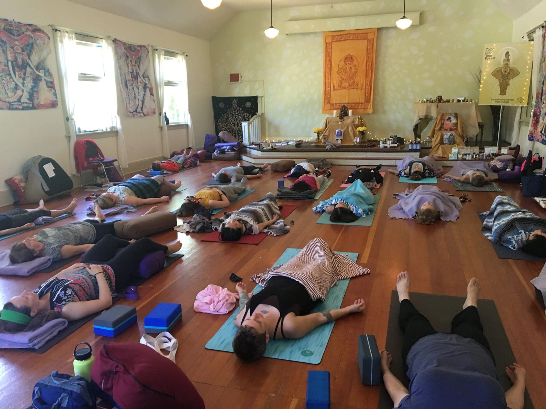 Sarasvati Foundations cohort resting in savasana on warm wood floors